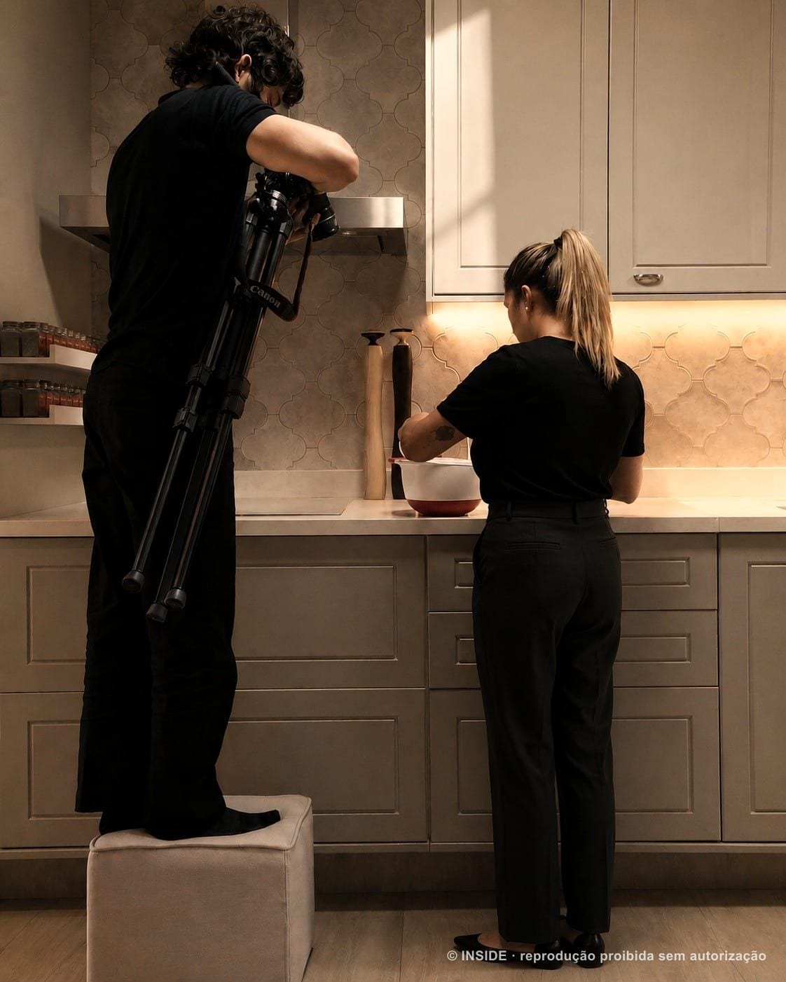 Equipe da INSIDE gravando um vídeo na cozinha de um apartamento já entregue, com o cinegrafista sobre um banco e a moradora cozinhando, acervo INSIDE