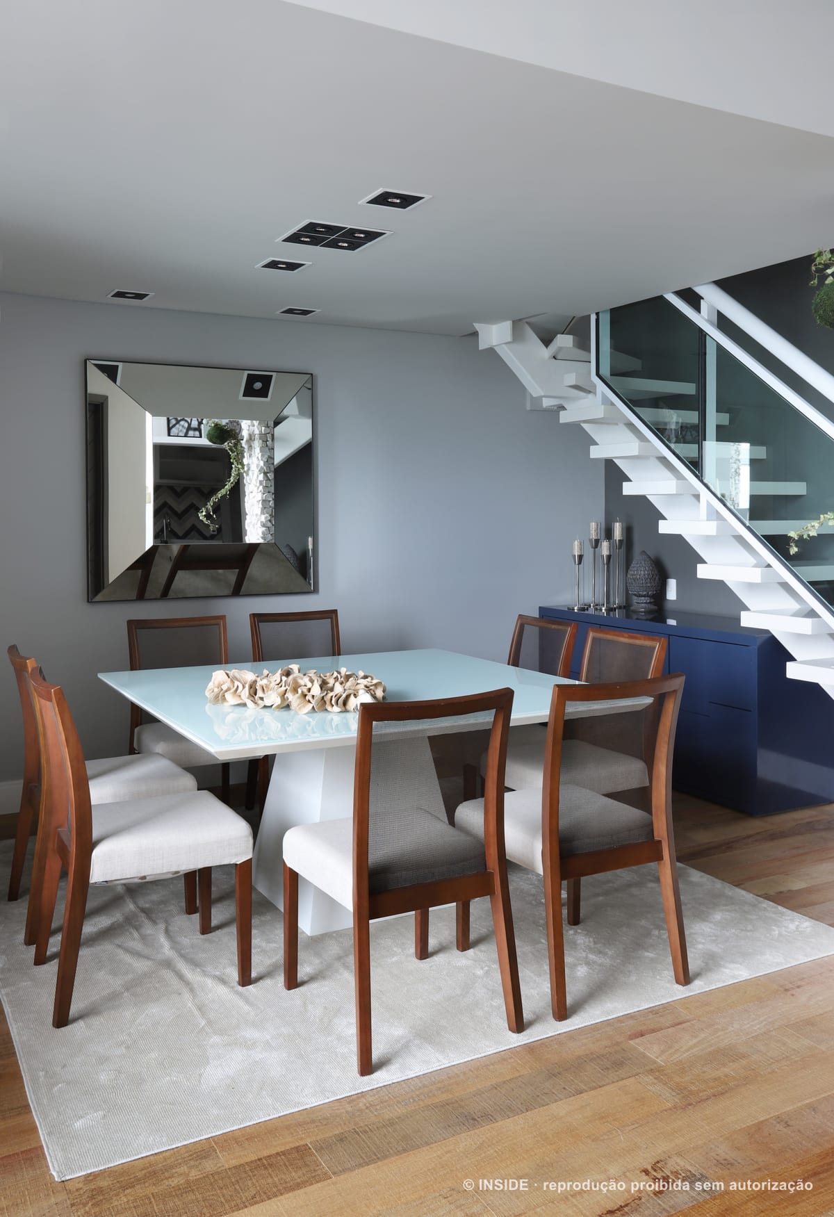 Sala de jantar com mesa quadrada de tampo claro e cadeiras de madeira, aparador azul e escada metálica ao fundo, apartamento Brooklin-PE, foto Mariana Orsi, acervo INSIDE