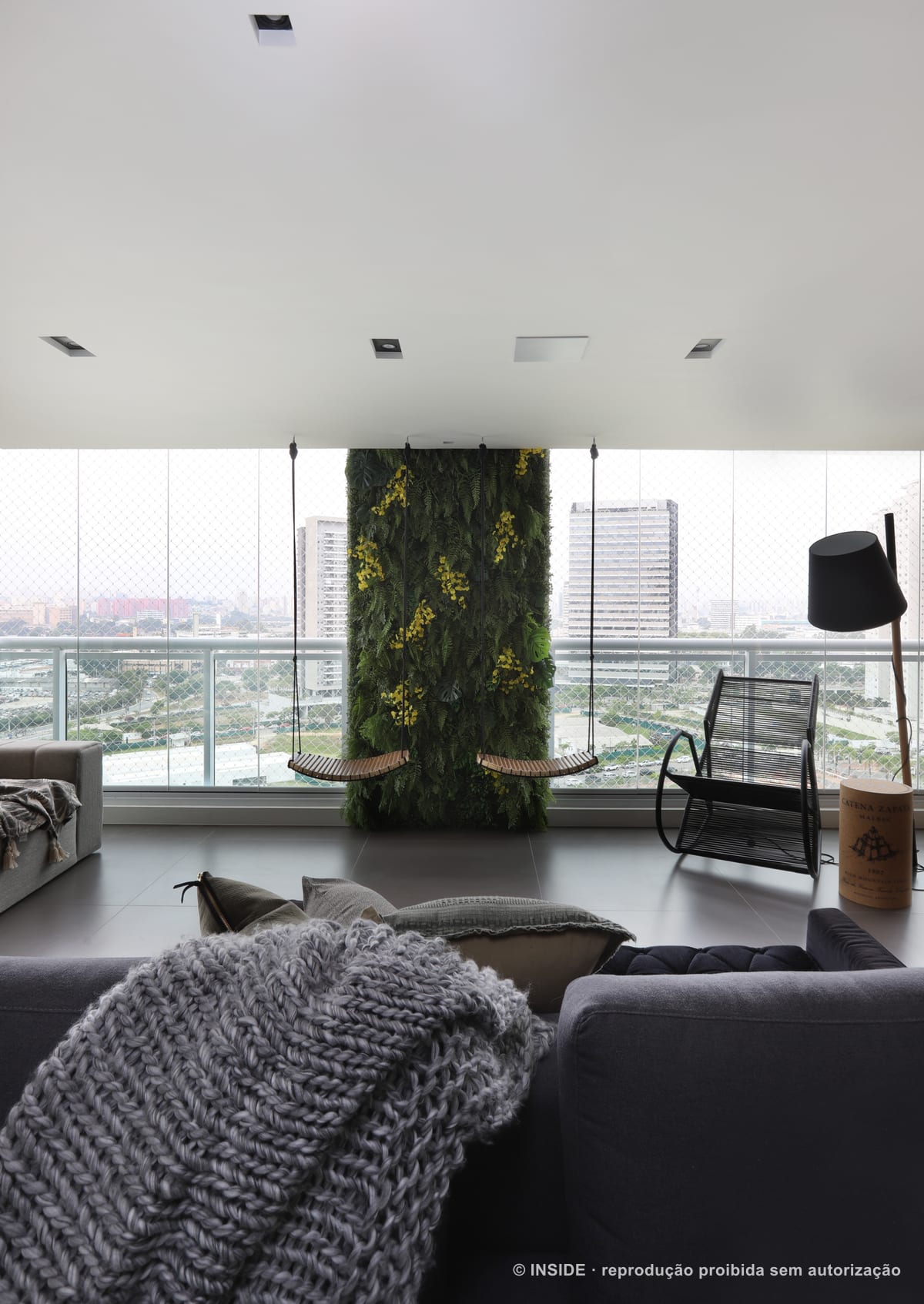 Varanda integrada com jardim vertical florido, balanço suspenso, poltrona de balanço e o horizonte de São Paulo pela vidraça, apartamento Perdizes-DB, foto Mariana Orsi, acervo INSIDE