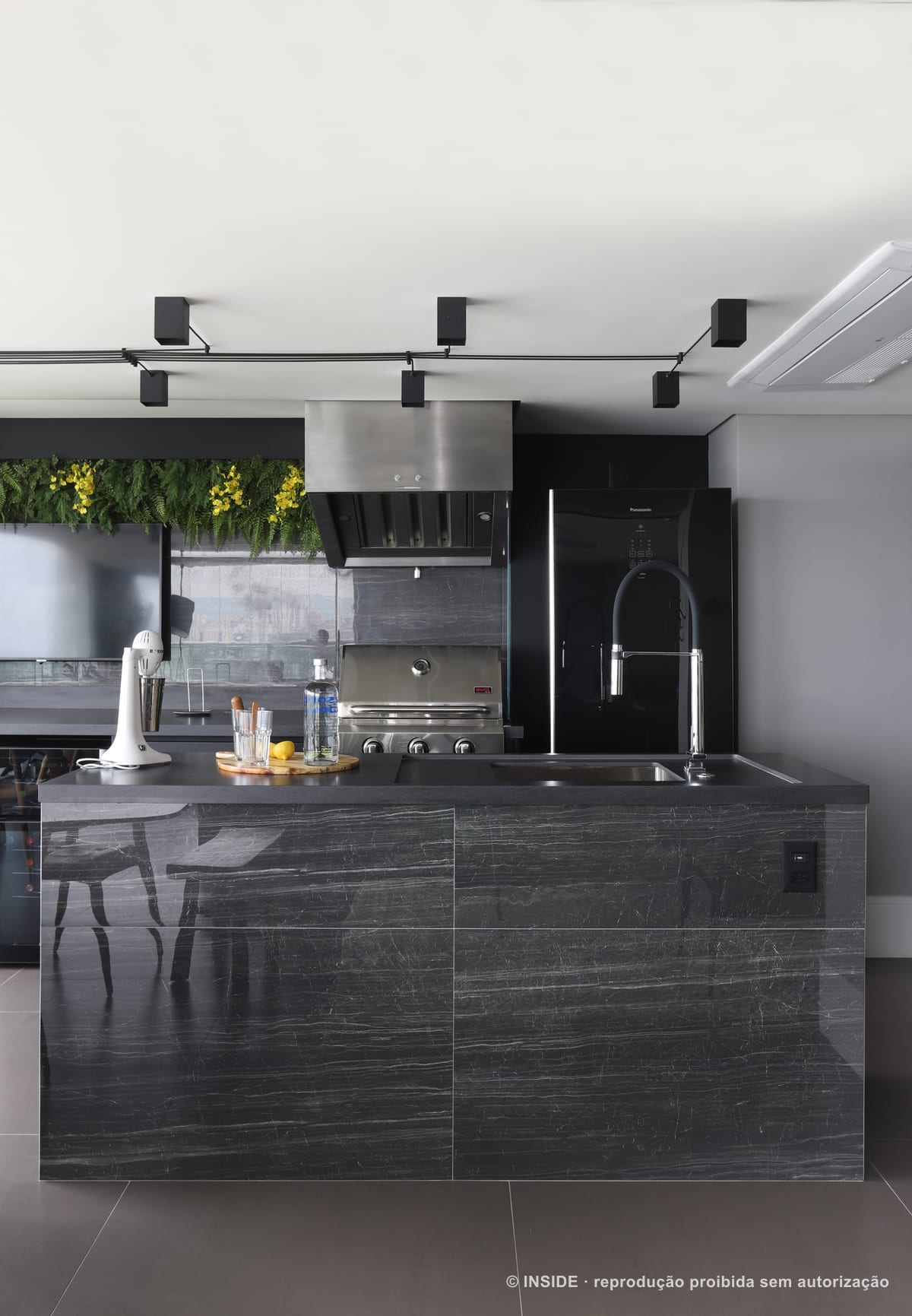 Bancada gourmet com cooktop, coifa de inox e armários escuros, com o jardim vertical ao fundo, apartamento Perdizes-DB, foto Mariana Orsi, acervo INSIDE