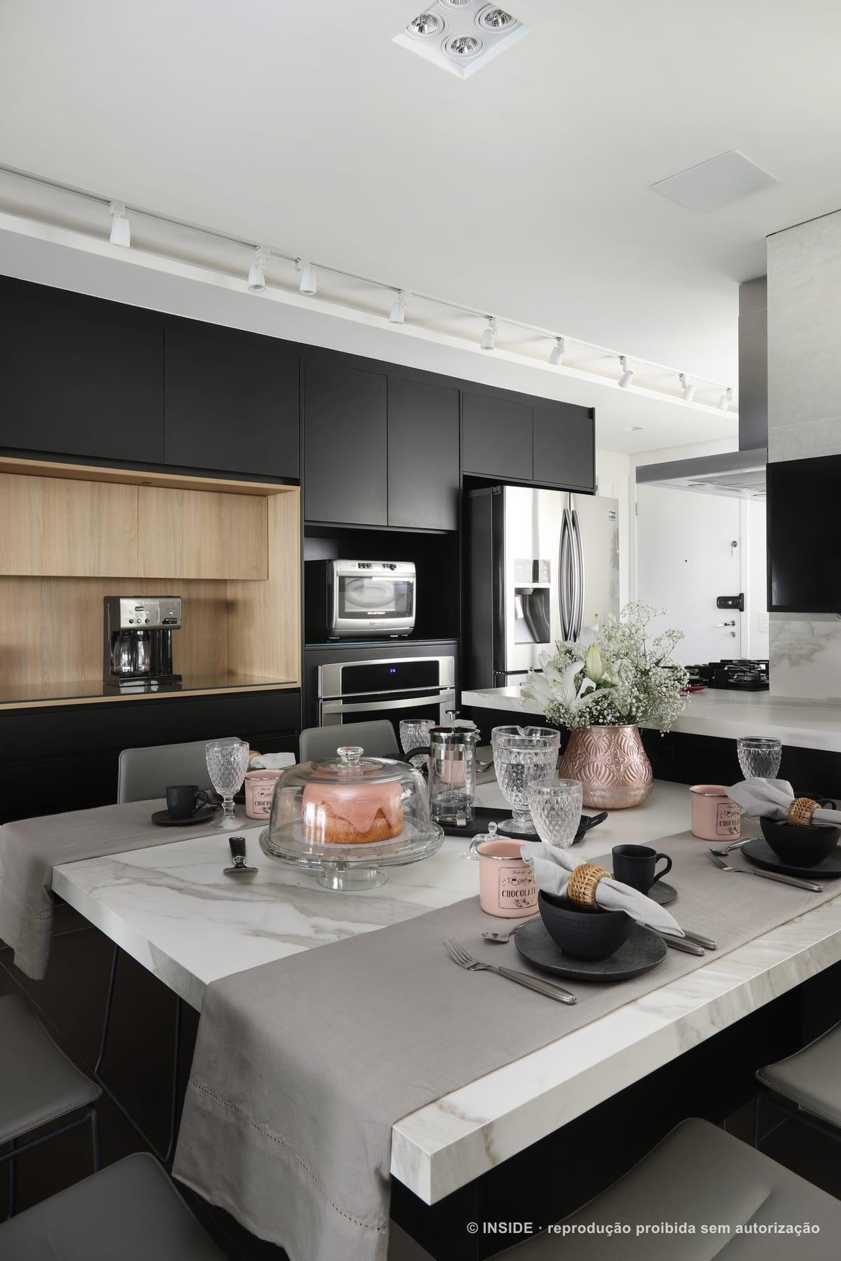 Cozinha com marcenaria preta e amadeirada, forno e micro-ondas embutidos, bancada de mármore com louças e taças, apartamento Perdizes-DB, foto Mariana Orsi, acervo INSIDE