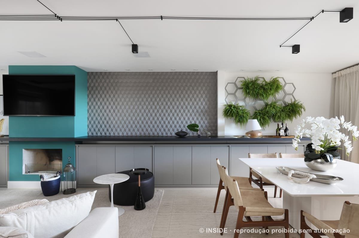 Living e sala de jantar integrados, com lareira revestida em verde-azulado, sofá em L claro e painel de vegetação em nichos hexagonais ao fundo, Vila Monumento-FC, foto Mariana Orsi, acervo INSIDE