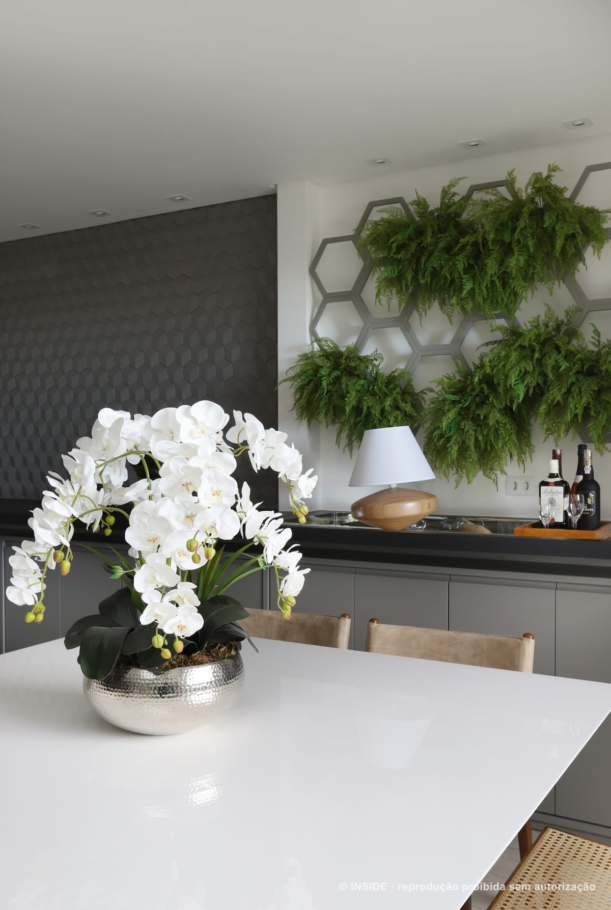 Aparador do jantar com orquídeas brancas, luminária de mesa e o painel de folhagens em nichos hexagonais na parede, Vila Monumento-FC, foto Mariana Orsi, acervo INSIDE