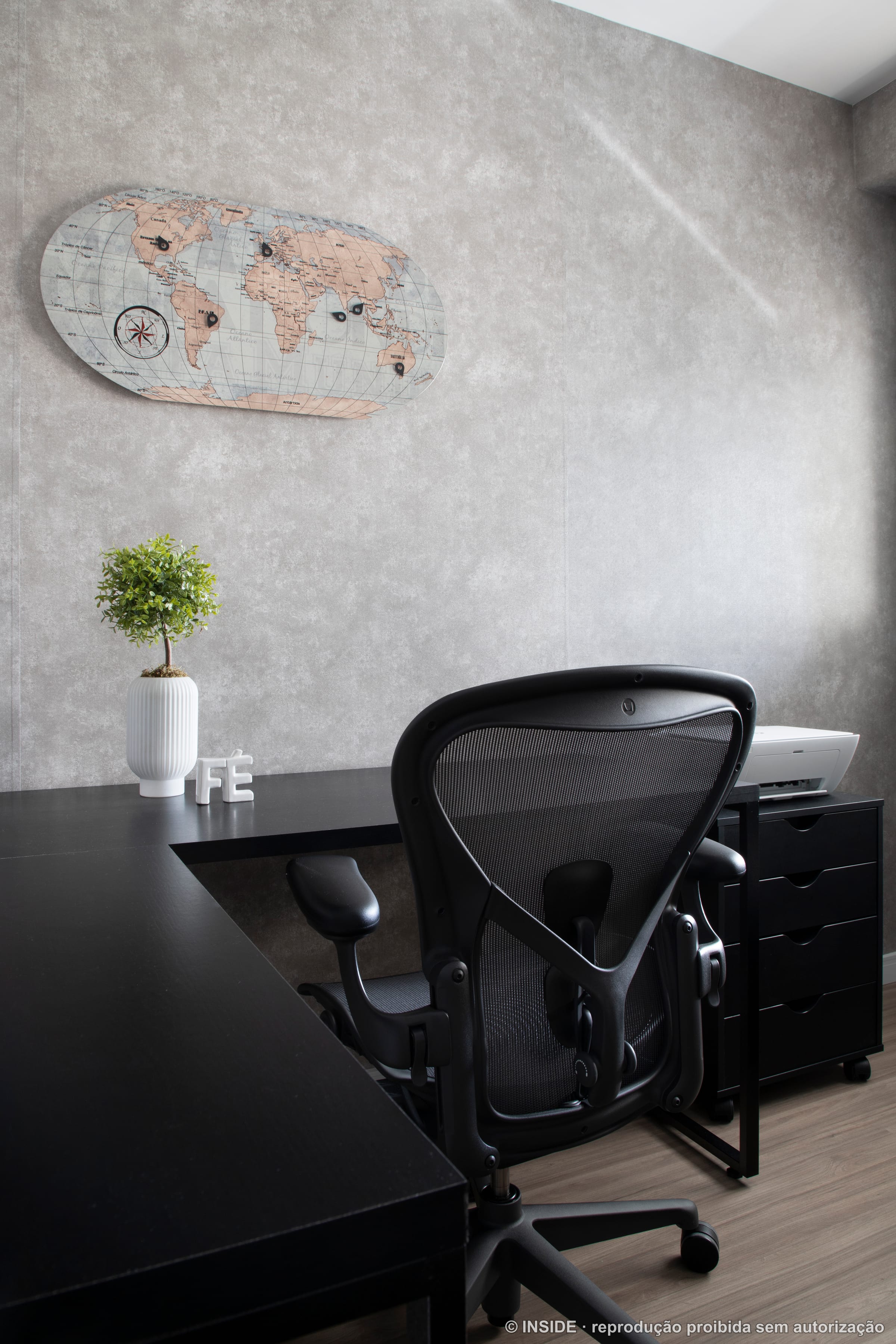 Home office com mesa em L preta, cadeira Aeron e mapa-múndi na parede, projeto INSIDE