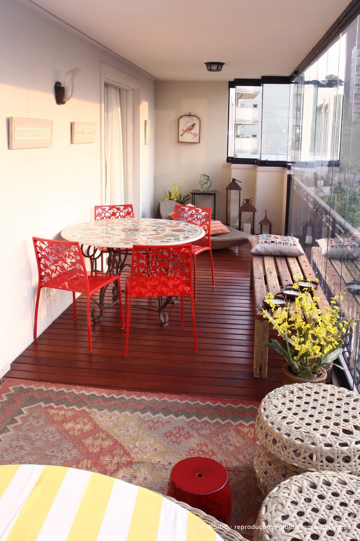 Pacaembu-RA: a varanda envidraçada com deck de madeira, mesa de mosaico e cadeiras vermelhas, acervo INSIDE