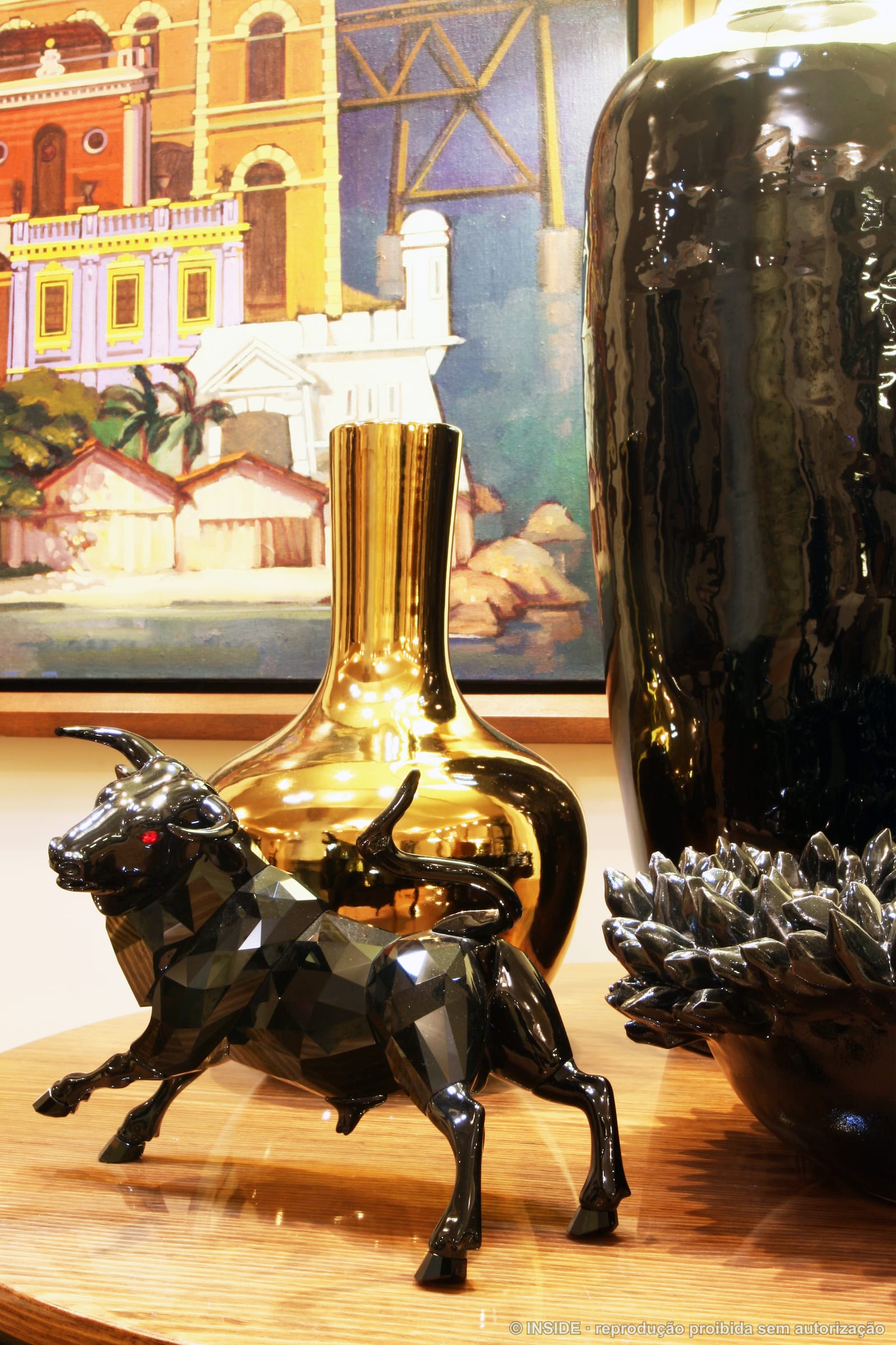 Close do touro em cristal facetado preto sobre o console, com vaso dourado e o quadro do casario ao fundo, projeto INSIDE