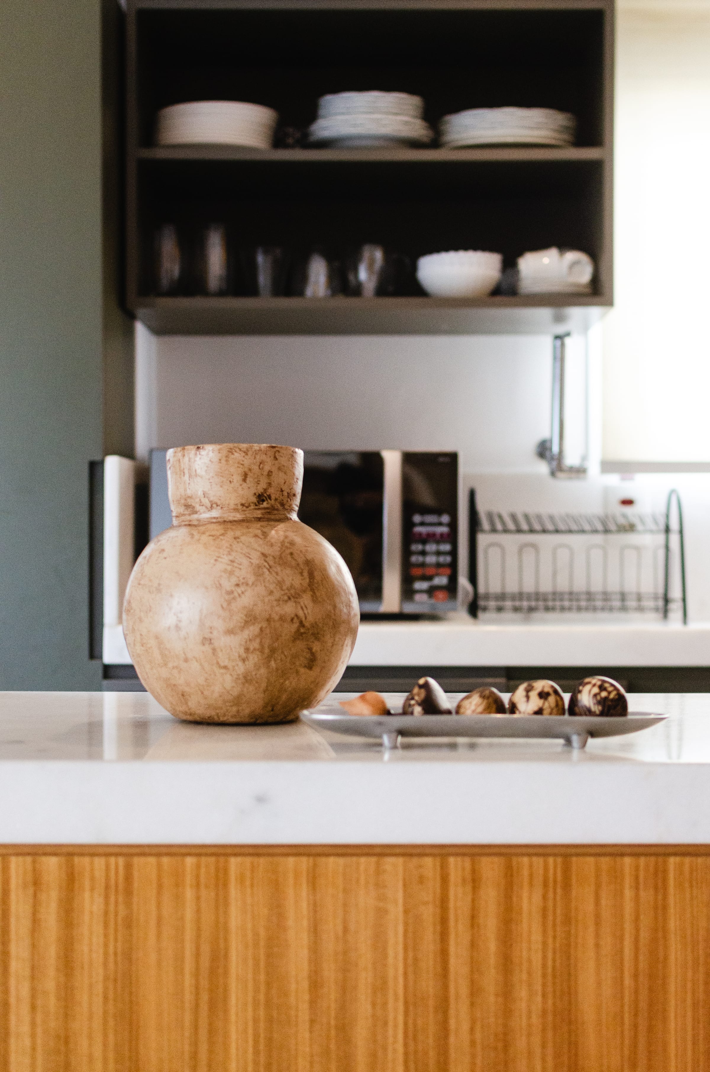 Detalhe de bancada com vaso artesanal em terracota e vista para cozinha com prateleiras abertas ao fundo, projeto INSIDE